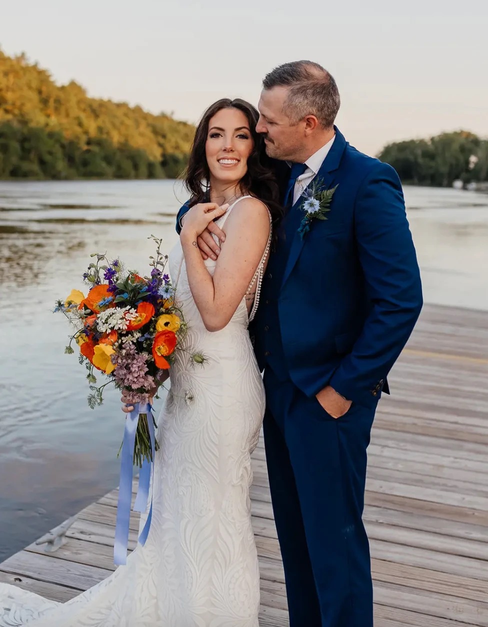 The newlyweds embracing on the dock at golden hour, the Kennebec River behind them